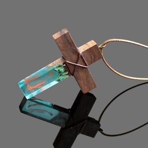 May include: A wooden cross pendant with a blue and orange resin inlay. The pendant is attached to a brown cord.