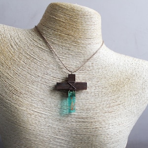 May include: A brown wooden cross pendant with a teal blue resin inlay. The pendant is on a brown cord necklace.