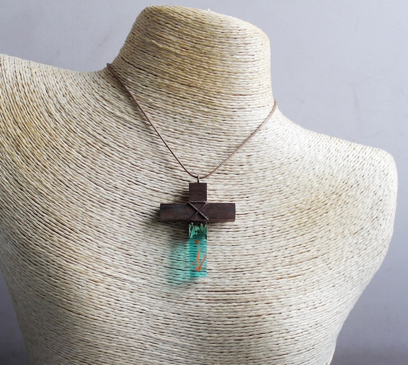 May include: A brown wooden cross pendant with a teal blue resin inlay. The pendant is on a brown cord necklace.