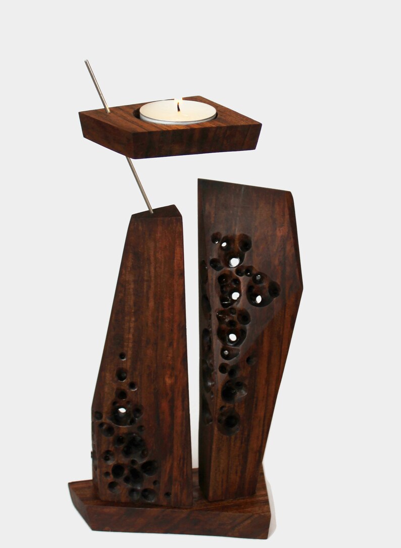 Peut inclure: Un bougeoir en bois avec un design g&eacute;om&eacute;trique. Le bougeoir a un petit porte-bougie rond sur le dessus et deux pi&egrave;ces rectangulaires hautes sur le dessous. Le bois est brun fonc&eacute; et a une finition naturelle et rustique.