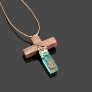 May include: A wooden cross pendant necklace with a green and orange resin inlay. The cross is tied with brown string and hangs from a brown leather cord.