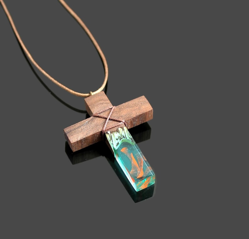 May include: A wooden cross pendant necklace with a green and orange resin inlay. The cross is tied with brown string and hangs from a brown leather cord.