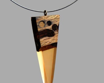 May include: A wooden pendant with a geometric shape, featuring a brown and black wood design with a clear resin layer. The pendant is attached to a black cord.