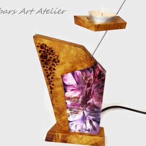 Peut inclure: Un bougeoir en bois unique au design g&eacute;om&eacute;trique. La base et la partie sup&eacute;rieure sont en bois clair, avec une section en r&eacute;sine violette et blanche. Une petite bougie est plac&eacute;e dans un support en bois au-dessus.