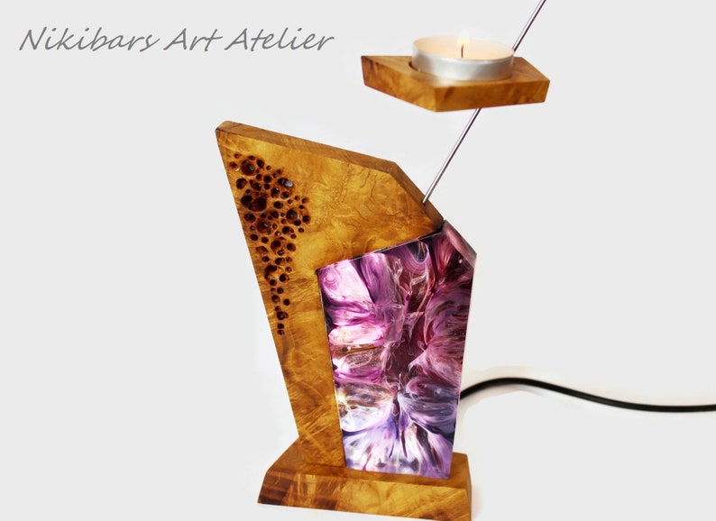 Peut inclure: Un bougeoir en bois unique au design g&eacute;om&eacute;trique. La base et la partie sup&eacute;rieure sont en bois clair, avec une section en r&eacute;sine violette et blanche. Une petite bougie est plac&eacute;e dans un support en bois au-dessus.