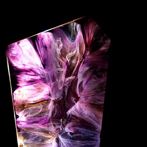Peut inclure: Pi&egrave;ce d'art abstraite en r&eacute;sine avec des pigments violets, blancs et dor&eacute;s tourbillonnants. L'&oelig;uvre est enferm&eacute;e dans une forme g&eacute;om&eacute;trique claire, cr&eacute;ant un effet visuel unique. Le fond est noir uni.