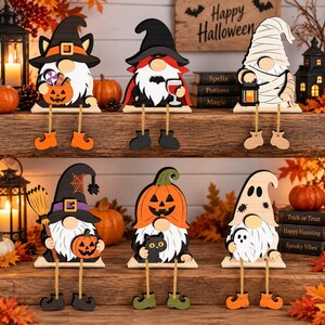 Könnte beinhalten: Sechs hölzerne Wichtelfiguren für Halloween. Die obere Reihe zeigt eine Hexe mit Kürbiseimer, einen Vampir mit Weinglas und eine Mumie mit Laterne. Die untere Reihe zeigt eine Hexe mit Besen, einen Wichtel mit Kürbiskopf und schwarzer Katze sowie ein Gespenst.