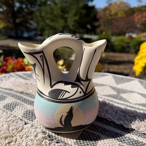 May include: A cream-colored ceramic wedding vase with a double-spout handle. The body features a painted scene of a black wolf howling at a full moon against a pastel pink and blue gradient background, with black geometric line art on the upper section.