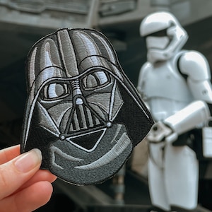 May include: A black and gray embroidered Darth Vader patch with a white Stormtrooper in the background.