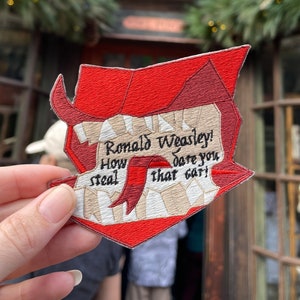 May include: A red and white embroidered patch with the text "Ronald Weasley! How dare you steal that car!" The patch is shaped like a wizard's hat.