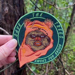 May include: A green, round embroidered patch with the text "The Trees Save Ewoks for Endor" and a cartoon image of an Ewok with a red hood.