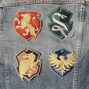 May include: Four embroidered patches featuring the Hogwarts house crests: Gryffindor (lion), Slytherin (snake), Hufflepuff (badger), and Ravenclaw (eagle). The patches are on a blue denim jacket.
