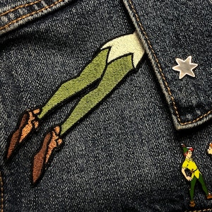 May include: A denim jacket with an embroidered Peter Pan patch, a silver star pin, and two enamel pins of Peter Pan and Wendy from the Disney movie.