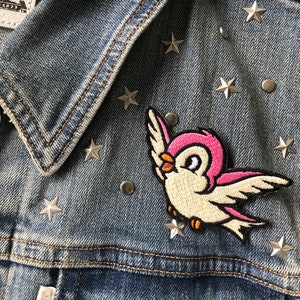May include: A denim jacket with silver star-shaped embellishments and a pink and white embroidered bird patch.