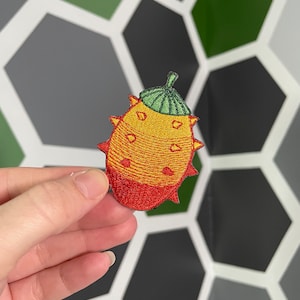 Könnte beinhalten: Ein gestickter Aufnäher mit einem Kiwano-Melonenmotiv in Rot und Gelb, einem grünen Stiel und Stacheln.
