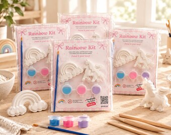 May include: Three clear plastic-wrapped Rainbow Kit sets, each containing a white plaster rainbow and unicorn figure, a blue paintbrush, and three small paint pots in blue, pink, and purple. The packaging features pink text and bows.