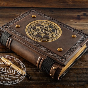 K&ouml;nnte beinhalten: Ein handgefertigtes, braunes, ledergebundenes Buch mit goldenen Akzenten und einem detaillierten kreisf&ouml;rmigen Design auf dem Einband. Das Buch hat goldfarbene Seiten und wird von einem goldenen Stift begleitet. Das Bild enth&auml;lt ein Logo "aLexLibris".