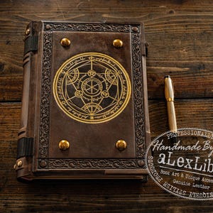 K&ouml;nnte beinhalten: Ein braunes Lederbuch mit einem goldenen, kreisf&ouml;rmigen Design auf dem Einband und goldenen Nieten. Ein goldener Stift liegt neben dem Buch. Ein handgefertigtes Produkt.