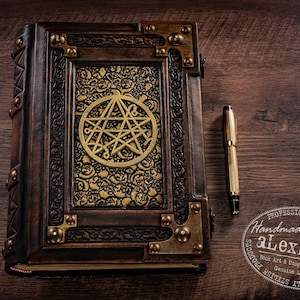 May include: A handcrafted, leather-bound journal with a gold pentagram design on the cover. The journal features ornate metal corner accents and a matching gold pen. The cover is dark brown with gold accents.