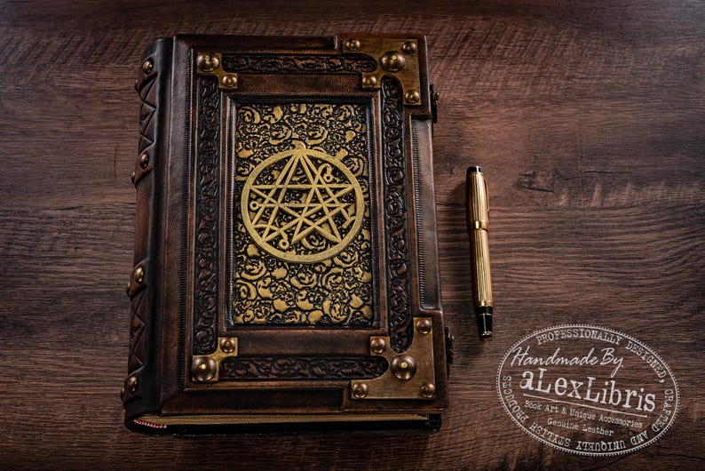May include: A handcrafted, leather-bound journal with a gold pentagram design on the cover. The journal features ornate metal corner accents and a matching gold pen. The cover is dark brown with gold accents.