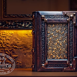 May include: A handcrafted leather book with intricate embossed floral patterns in gold and brown. The book has a decorative frame and metal accents. The text "Handmade By aLexLibris" is visible on the image.