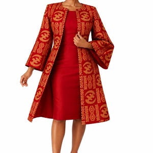 May include: A solid red knee-length dress paired with a long-sleeved open coat. The coat features a repeating gold geometric and circular pattern on a red background, with wide sleeves and a structured fit that reaches below the knees.