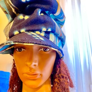 May include: A navy blue and patterned bucket hat with a brim. The hat features a mix of blue, yellow, and white accents. The hat is worn by a mannequin with brown skin and red curly hair.