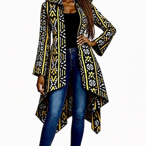 May include: A hooded duster coat with a black, yellow, and white geometric pattern. The coat has long sleeves and a high-low hemline. The person is wearing blue jeans and black heels. The coat is a statement piece.