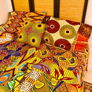 May include: A colorful patchwork quilt with a variety of African print fabrics in yellow, orange, red, blue, and brown. The quilt is made up of different patterns and designs, including geometric shapes, floral motifs, and animal prints.