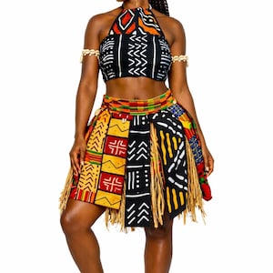 Pode incluir: Um traje de inspiração africana com um top halter e uma saia estampada. A parte superior é preta com desenhos geométricos brancos e detalhes em vermelho e laranja. A saia tem uma variedade de padrões e franjas.