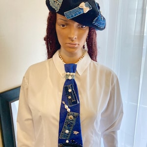 May include: A black beret and a blue denim tie, both adorned with denim patches, pearls, and decorative embellishments. The tie features denim pockets and various decorative elements. The beret has denim patches and bow accents.