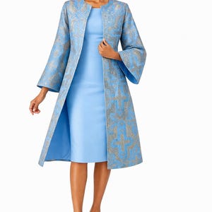 May include: A light blue dress and a matching long coat. The coat has a silver and blue patterned design and wide sleeves. The outfit is completed with gold-coloured heels, creating an elegant ensemble.