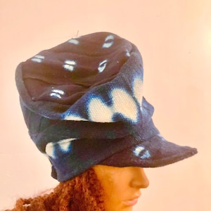 May include: A dark blue and white patterned hat with a brim. The hat has a unique design with white and blue tie-dye style patterns. The hat is made of a soft fabric and is displayed on a mannequin head.