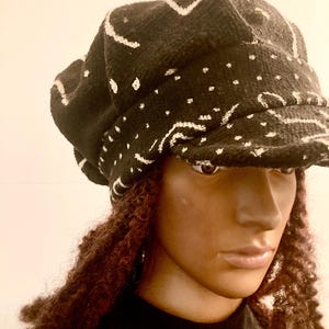 May include: A black and white patterned newsboy cap with a slightly curved brim. The cap is made of a soft, textured fabric.