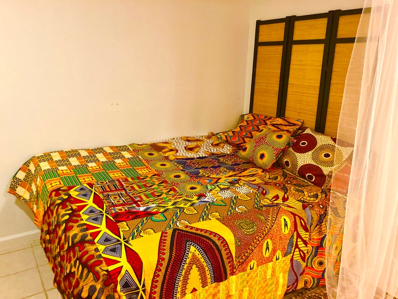 May include: A bed with a colorful patchwork quilt featuring yellow, red, green, and brown patterns. The bed has a headboard made of a wooden screen with black accents. There are several patterned pillows on the bed.