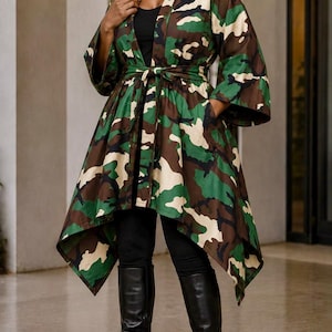 May include: A camouflage print kimono-style jacket featuring a high-low hemline, wide three-quarter length sleeves, and a matching fabric tie belt at the waist. The jacket is worn over a black top, black leggings, and black leather knee-high boots.