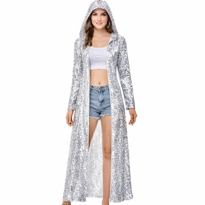 May include: A long, silver sequin hooded coat. The coat is open in the front and reaches the ankles. The sequins shimmer, reflecting light. The sleeves are long, and the hood is up. The coat is worn over a white top and denim shorts.