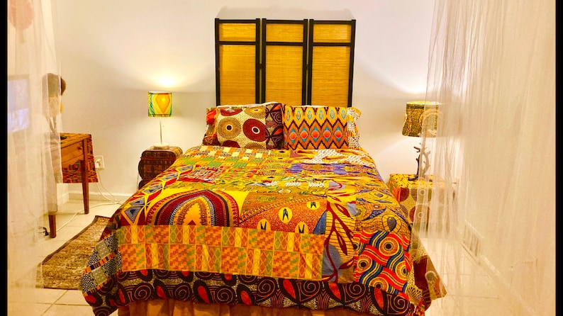 May include: A bed with a colorful African print duvet cover and matching pillows. The headboard is a wooden screen with a woven pattern. There are two bedside tables with lamps.