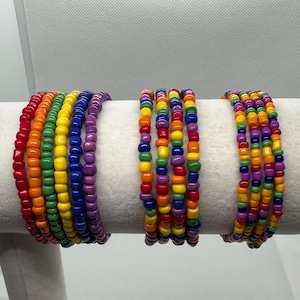 May include: Set of six rainbow beaded bracelets, each with a different color order. The bracelets are made of small, round beads in red, orange, yellow, green, blue, indigo, and violet.