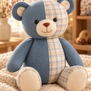 May include: A plush teddy bear featuring a split design with one side in solid blue fabric and the other in a blue and cream plaid pattern. The bear has a cream-colored muzzle, a brown stitched nose, a simple smile, and dark round eyes.