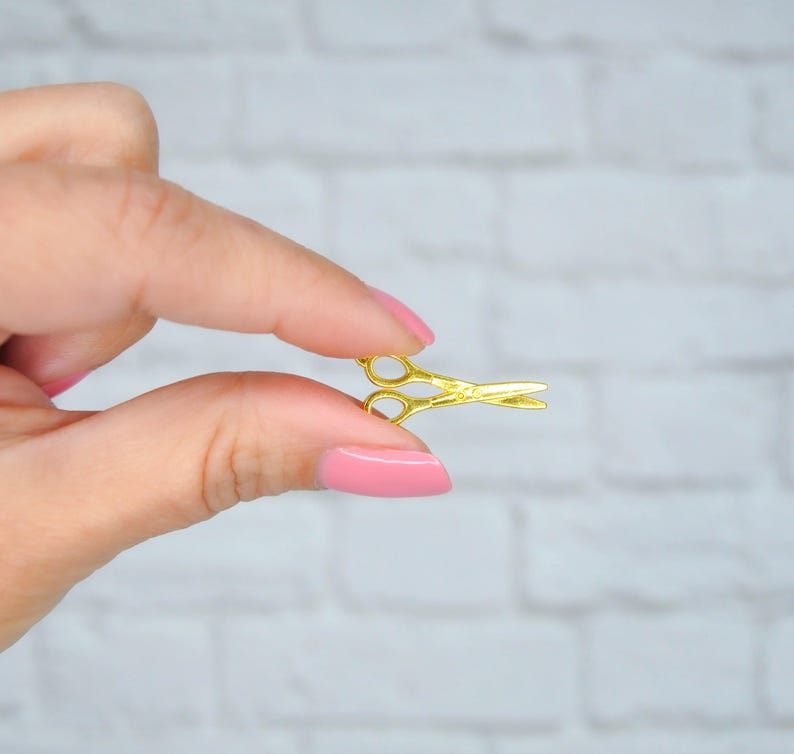 May include: A small gold-colored pair of scissors held between two fingers.