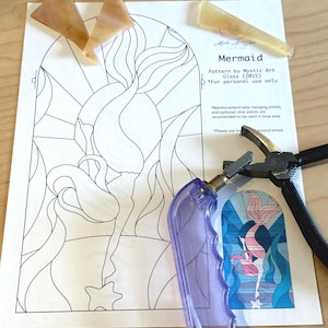 May include: A craft project featuring a "Mermaid" stained glass pattern by Mystic Art Glass. The image includes a pattern print, glass pieces, a glass cutter, and pliers. The pattern is for personal use only.