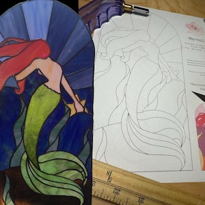 Può includere: Una sirena in vetro colorato con capelli rossi e una coda verde, circondata da alghe blu e verdi. L'immagine mostra anche un disegno a linea in bianco e nero di una sirena con il testo "Mermaid Pattern by Mystic Glass (2015) *For personal use only* *Recommended 13x24 in"