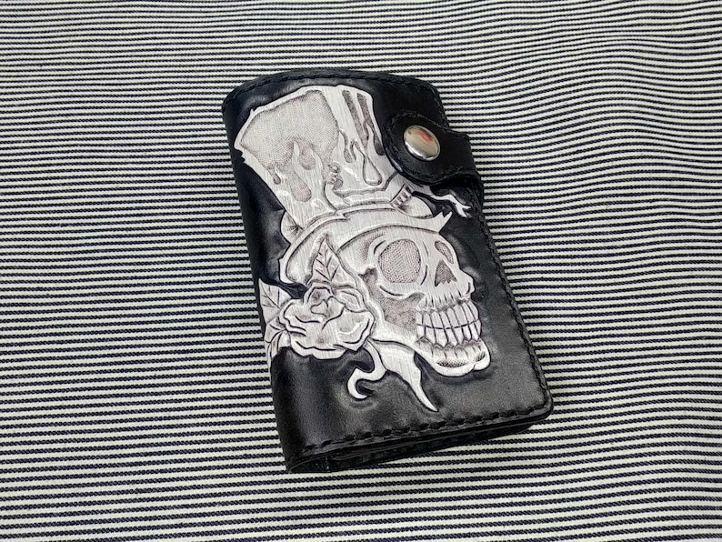 May include: Black leather wallet with a white skull and top hat design. The skull is wearing a top hat and has a rose behind it.
