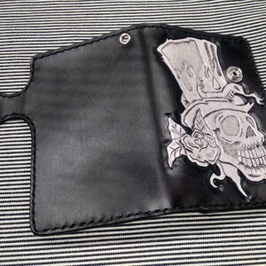 May include: Black leather wallet with a silver embossed design of a skull wearing a top hat and a rose.