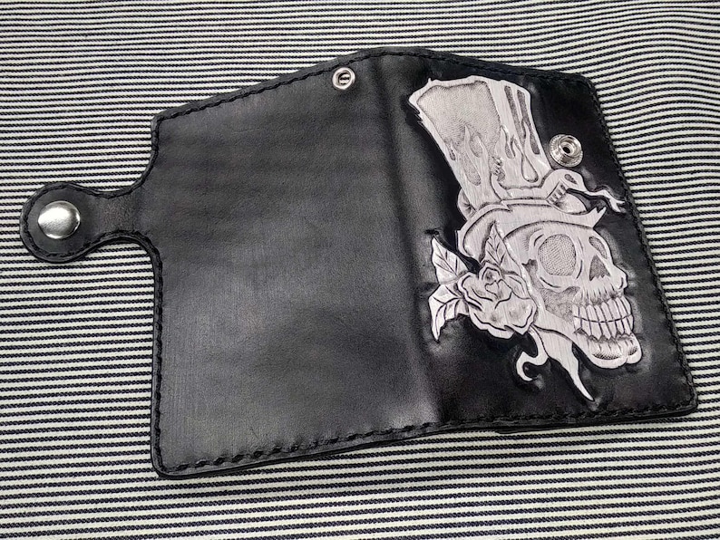 May include: Black leather wallet with a silver embossed design of a skull wearing a top hat and a rose.