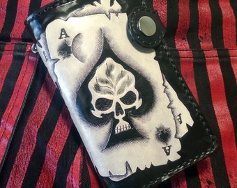 May include: Black leather wallet with a white ace of spades design featuring a skull. The wallet has a metal snap closure.