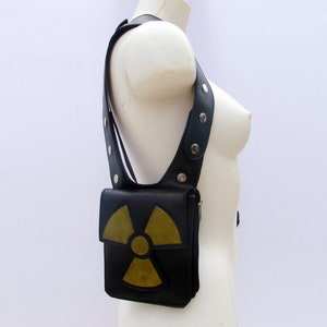 Puede incluir: Bolso de hombro de cuero negro con un símbolo de radiación amarillo y verde.