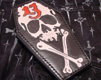 May include: Black leather wallet with a skull and crossbones design. The skull has a red number 13 on its forehead.