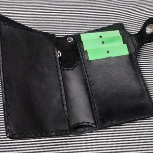 May include: A black leather wallet with multiple card slots and a snap closure. The wallet has a small pocket on the outside for a key or other small item.